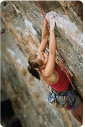 A rock climber reaching for the next hold on a steep cliff face.